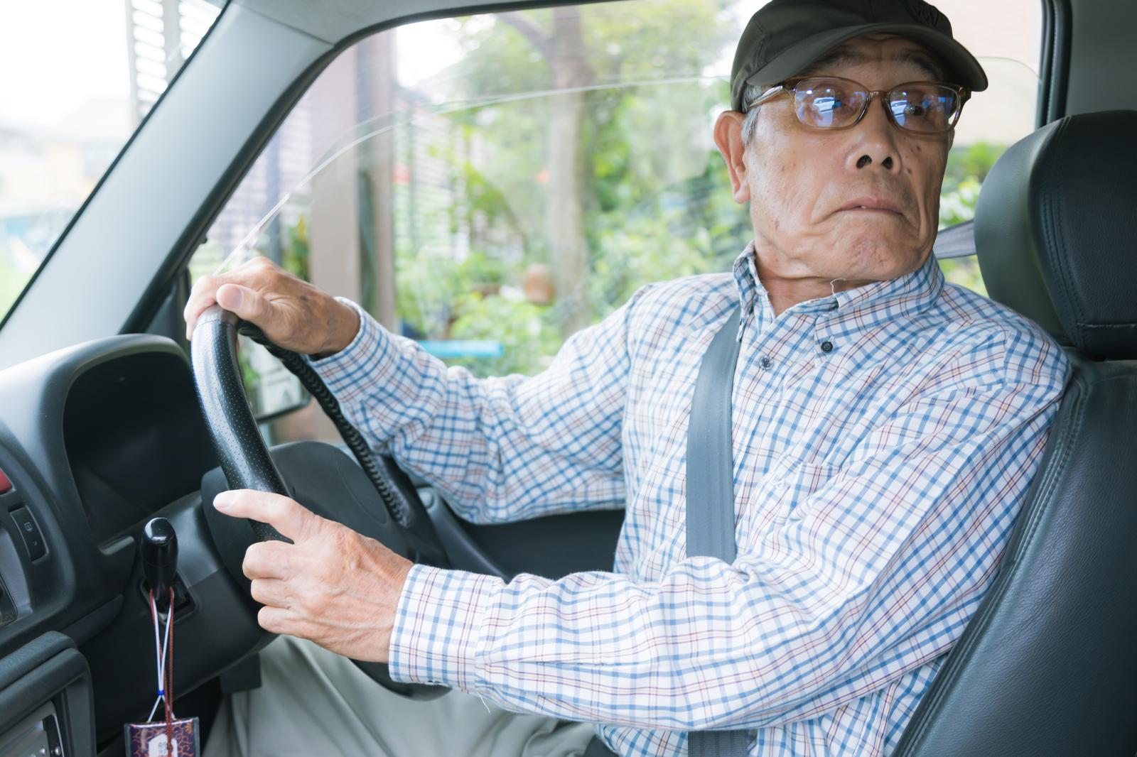 バック駐車で後方を確認しながらハンドルを握る眼鏡姿の高齢男性［モデル：まーちゃん］