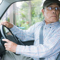 バック駐車で後方の音に反応する眼鏡姿の高齢男性の写真