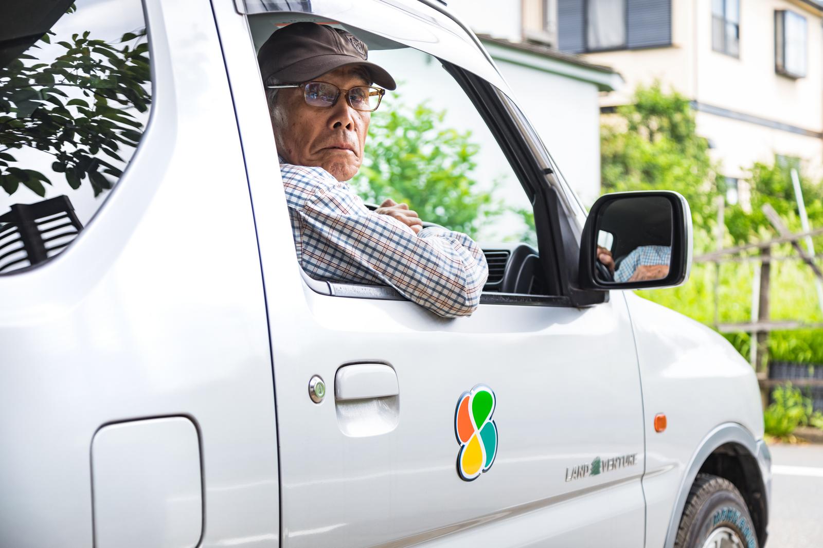 窓から身を乗り出して後方を確認しながらバックで駐車する眼鏡をかけた高齢男性［モデル：まーちゃん］