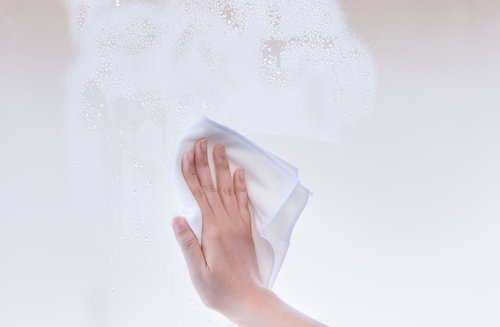 白い雑巾で窓ガラスを丁寧に乾拭きする手の清掃作業