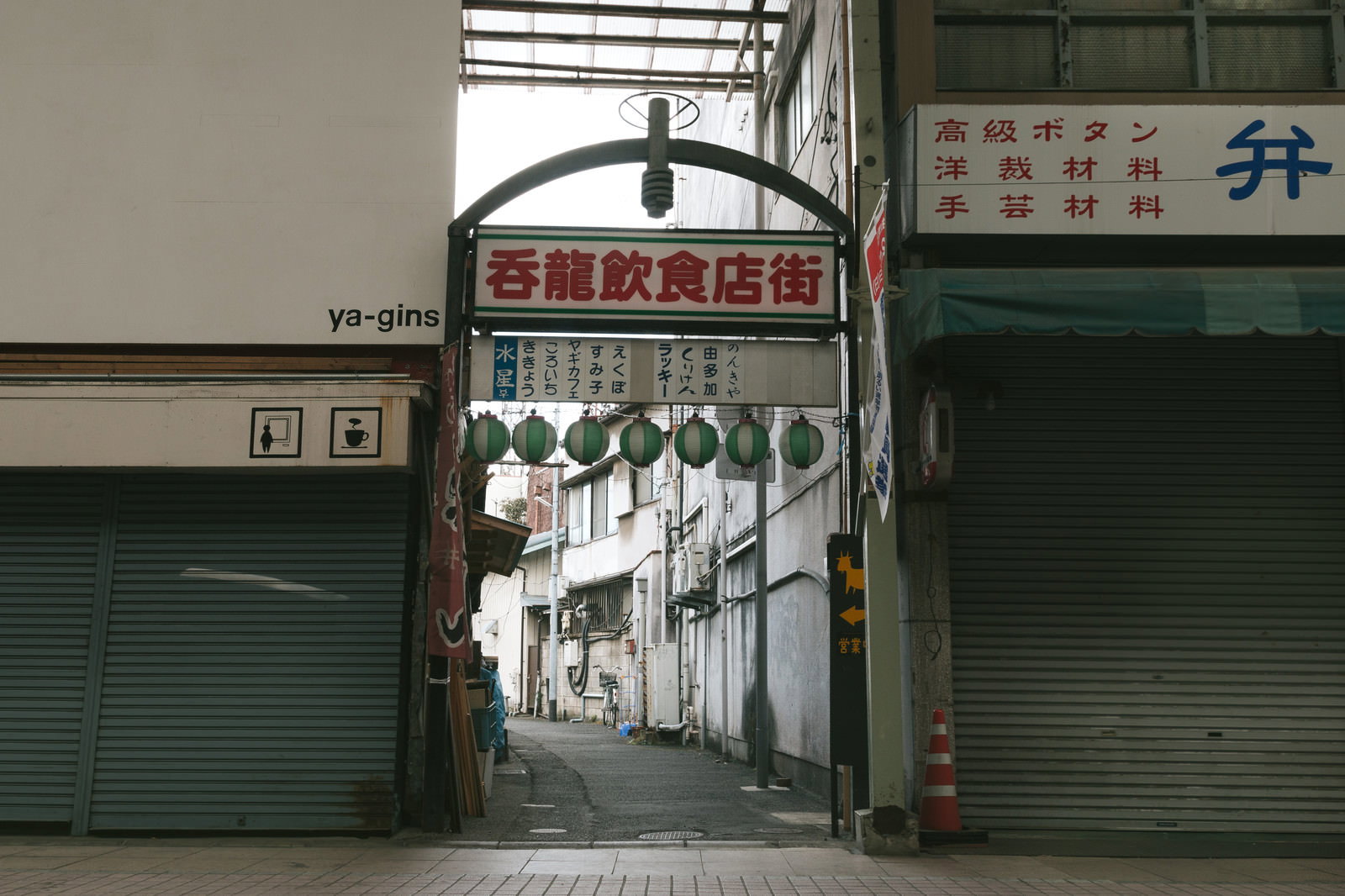 呑龍飲食店街の看板があるアーケード入り口と緑のシャッターが並ぶ商店街