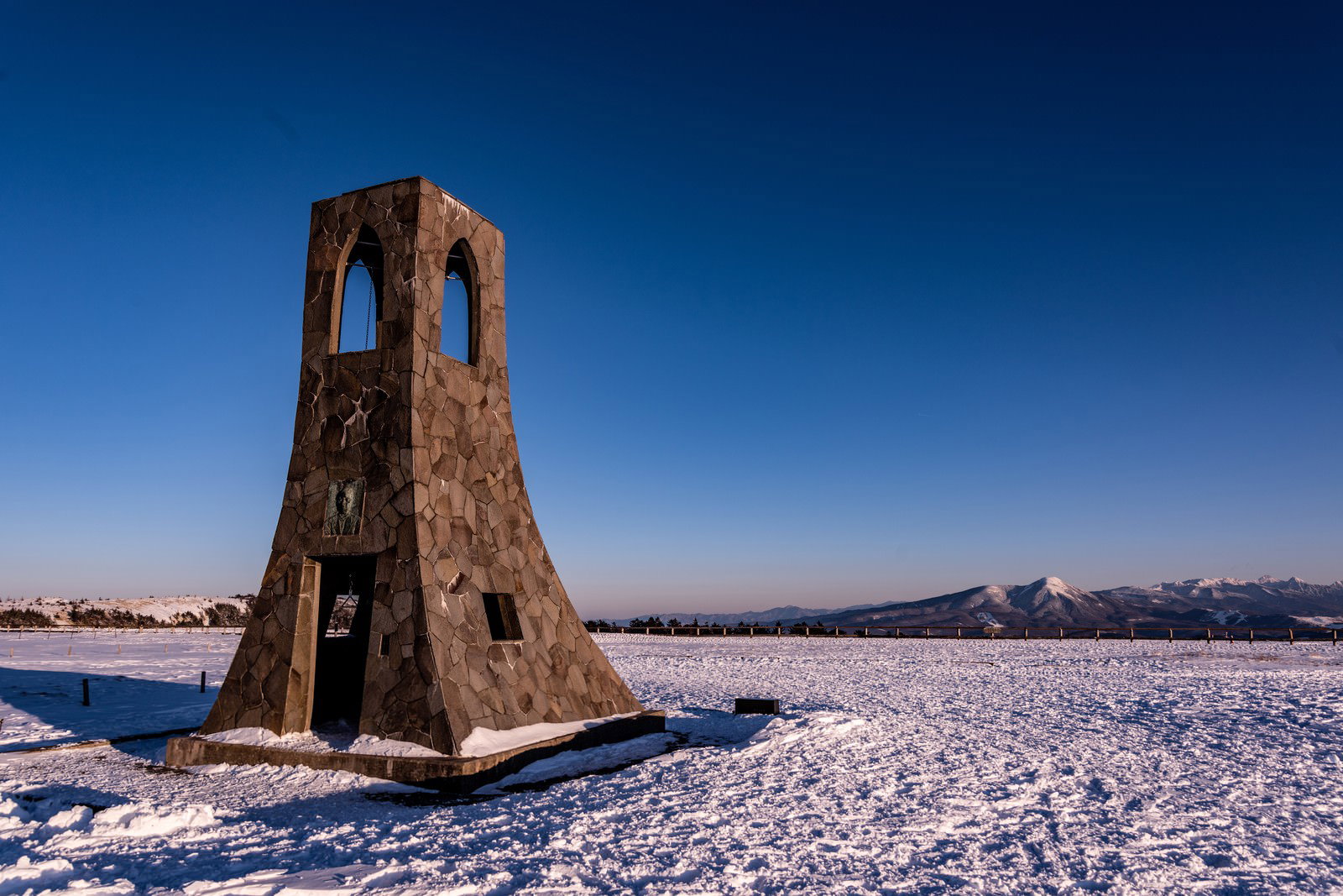 雪原に建つ茶色い木造の避難塔と青空の風景