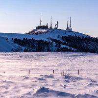 積雪の高台にそびえる複数アンテナの電波塔の写真