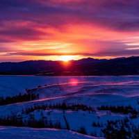 沈む夕日と広がる大雪原の冬風景、紫とオレンジの夕焼け空の写真