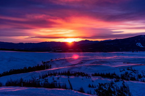 沈む夕日と広がる大雪原の冬風景、紫とオレンジの夕焼け空
