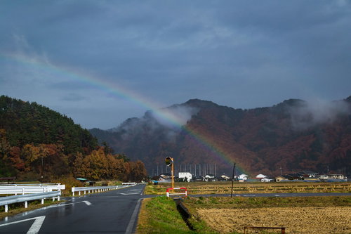 雨上がりの田んぼに架かる虹と山々の田舎風景