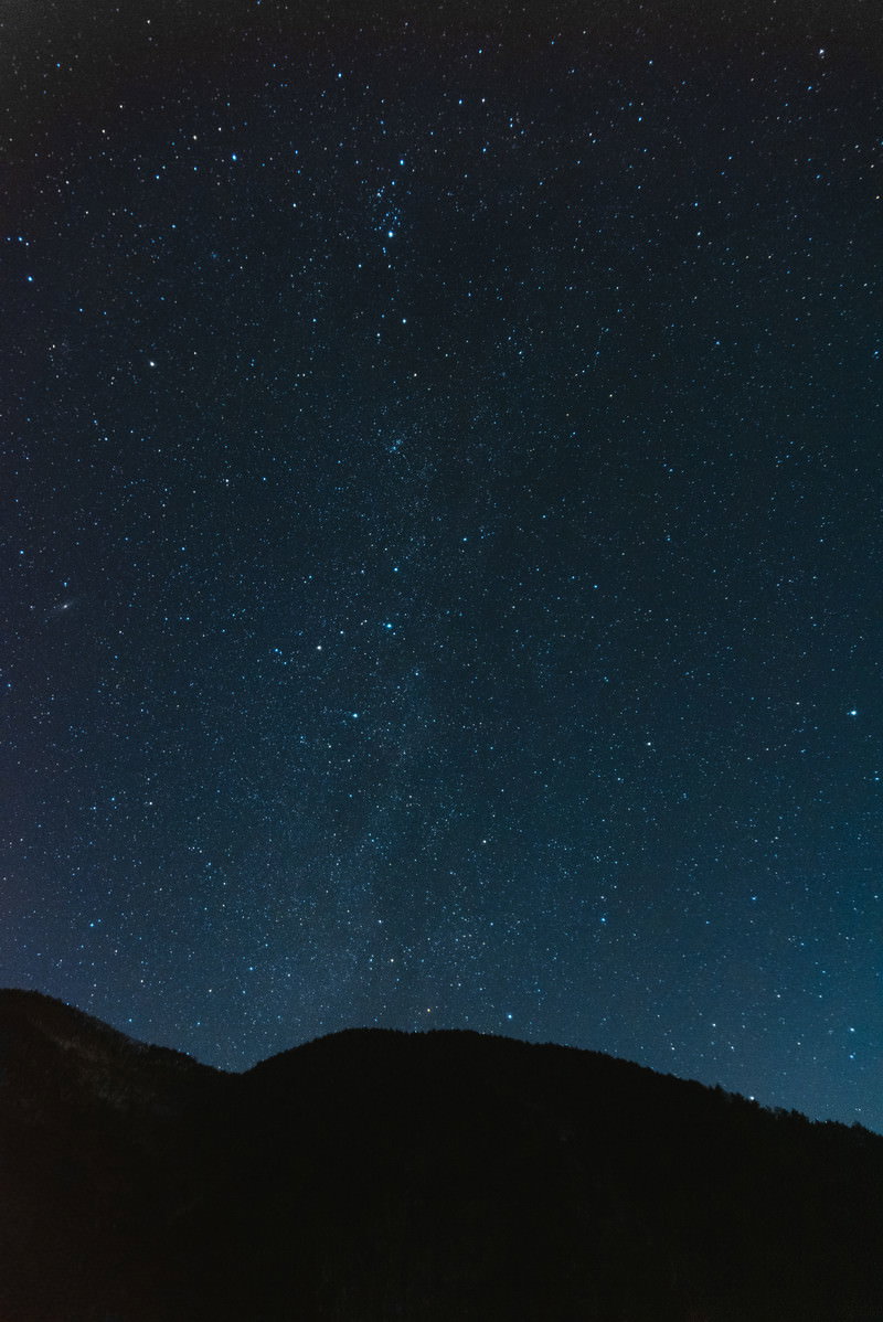 暗い夜空に星が輝き、手前に山のシルエットが見える星空の風景