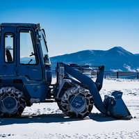 青空の下、雪原に停車中の除雪車と雪山、冬の道路管理の写真