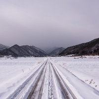 積雪した冬の田園を進む雪原の一本道と遠くの山々の写真