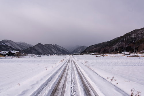 積雪した冬の田園を進む雪原の一本道と遠くの山々