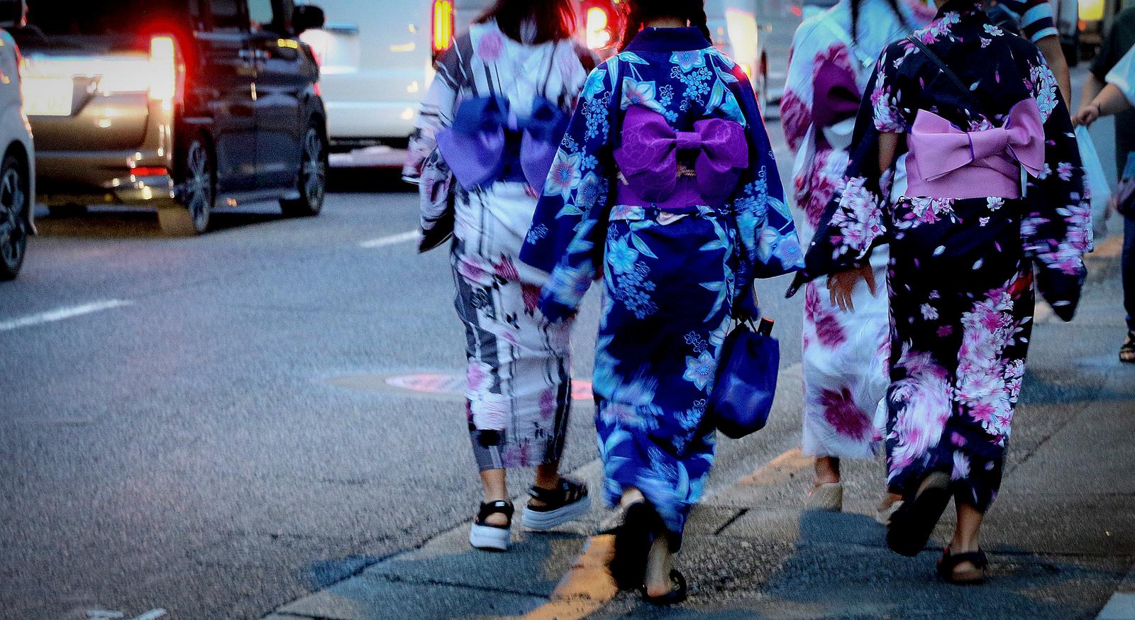 夕暮れの車道を浴衣姿で歩く女性たちの後ろ姿