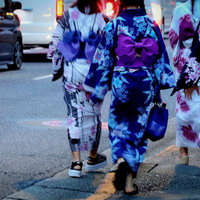 夏の夕暮れ、浴衣姿で街を歩く女性たちの後ろ姿の写真