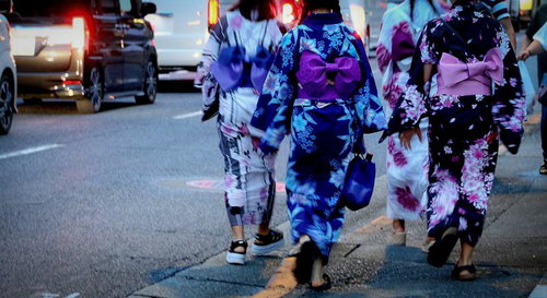 夏の夕暮れ、浴衣姿で街を歩く女性たちの後ろ姿