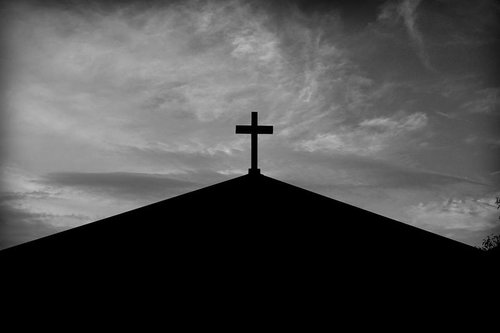 モノクロームに浮かぶ教会の十字架シルエットと雲の流れる空