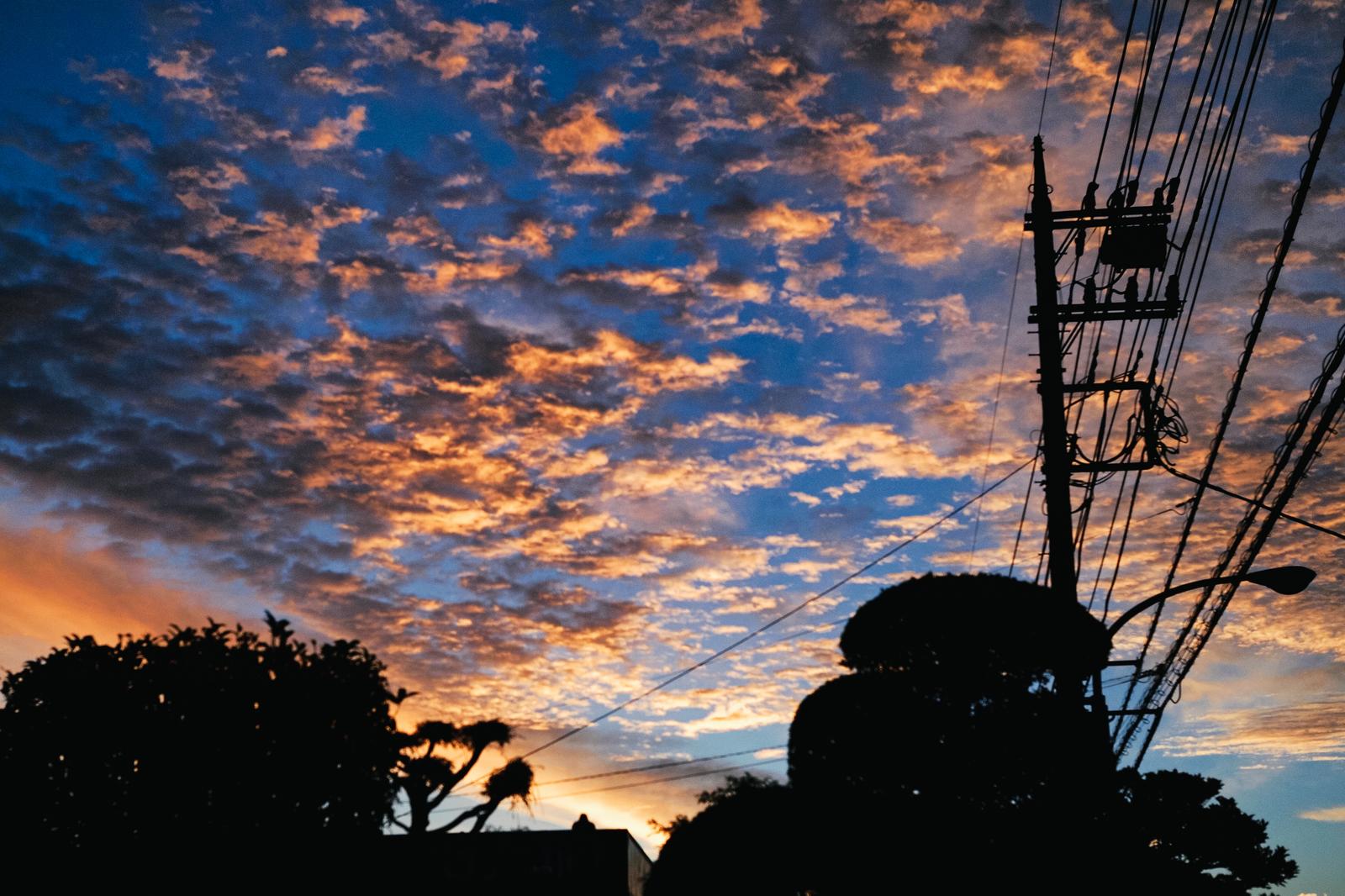 オレンジと青のグラデーション空に電柱と電線のシルエットが写る夕暮れの風景