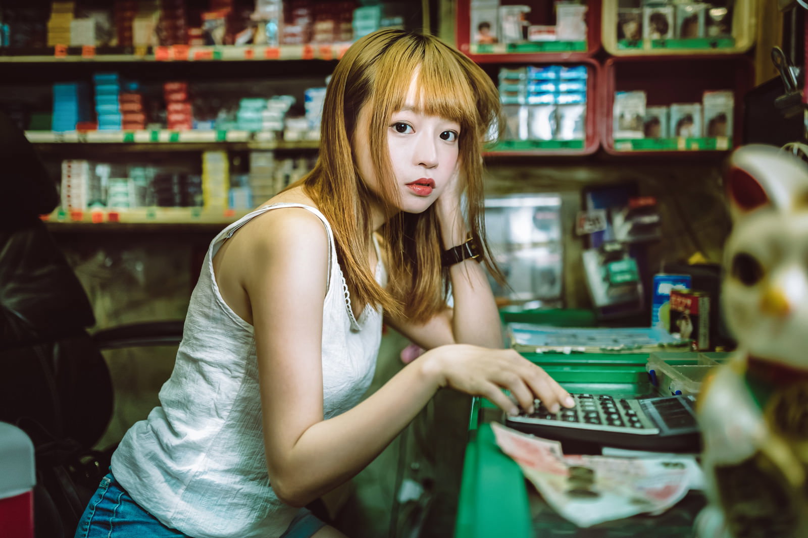 商店でレジ締め作業中に困った表情を見せるプリン髪の女性［モデル：まめち］
