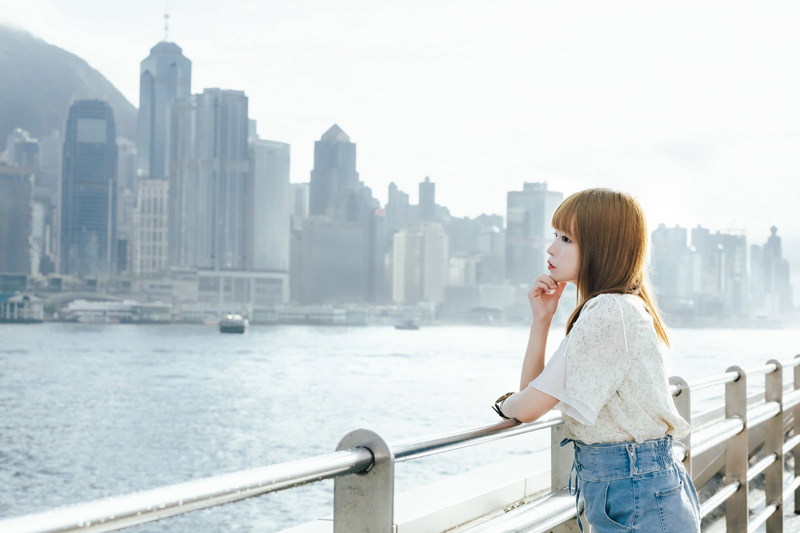 香港のビクトリアハーバーを見つめる白いシャツの女性［モデル：まめち］