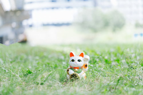 緑の芝生の上に置かれた白い幸運の招き猫、右手上げ