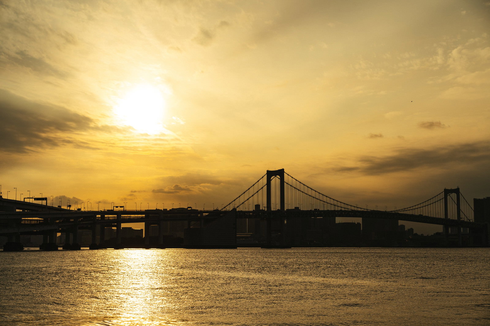 夕日が沈む夕暮れの海面に橋のシルエットが映る風景