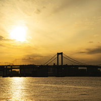 夕日に照らされた海面と橋のシルエット、夕焼けの風景の写真