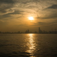 遠くの街並みから伸びる夕日のレイライン、水面に映る光の道の写真