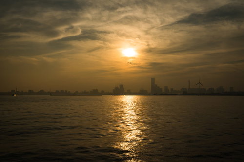 遠くの街並みから伸びる夕日のレイライン、水面に映る光の道