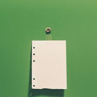 緑色の背景に白い紙と穴が開いた留め具付きストラップが置かれた写真の写真
