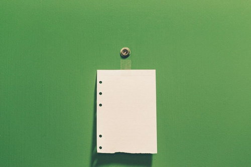 緑色の背景に白い紙と穴が開いた留め具付きストラップが置かれた写真