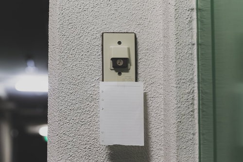 白い壁のベージュのスイッチカバーの下に貼られた白い紙のメモ