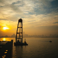 港から見る夕日と街並みのシルエット、水面に映る黄金色の光の写真