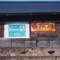 錆びて電話番号がほとんど見えなくなっている「マルフク」の看板の写真