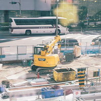 大阪の建築現場で油圧ショベルと通り抜けるバスの共演の写真
