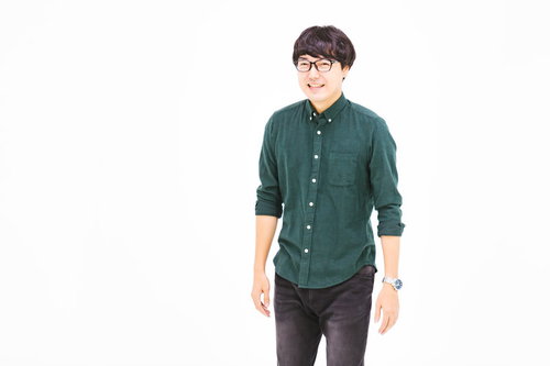 緑のシャツではにかむ猫背の男子エンジニア