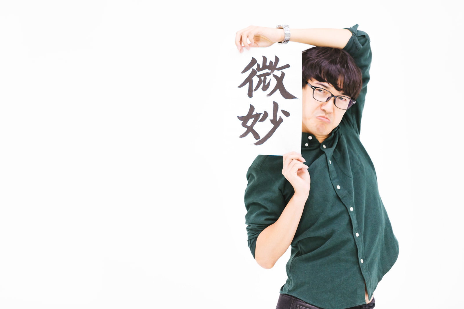 緑色のシャツを着た男性が困った表情で手を頬に当てている［モデル：真崎真幸］