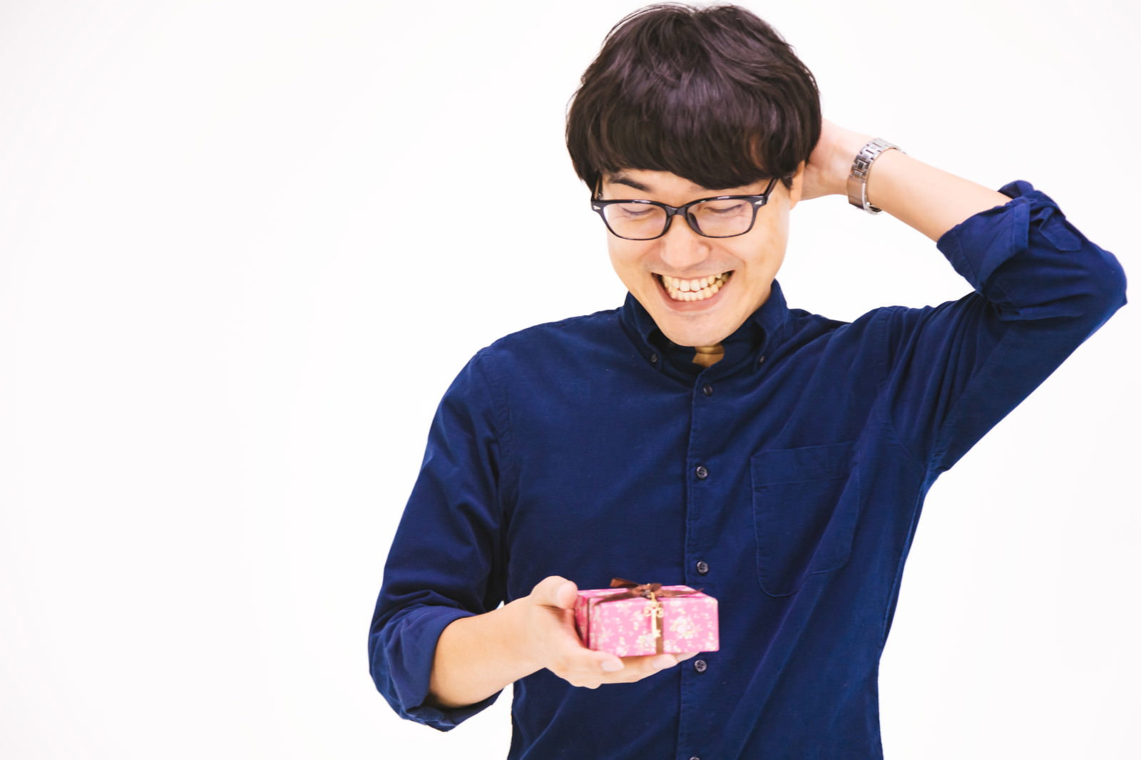 ピンクのプレゼントボックスを持ちながら照れるように頭を掻く眼鏡の男性［モデル：真崎真幸］