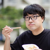 公園のベンチで牛丼をモグモグ食べる眼鏡男子の写真