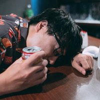 テーブルに突っ伏して酔い潰れた眼鏡男子のヤケ酒の写真