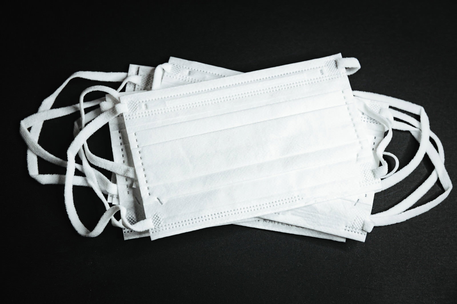 黒い背景に置かれた白いマスクが複数重なり紐が絡まった状態