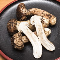 黒い皿に盛られた松茸を半分に割いた状態の食材の写真