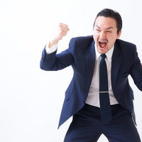 奇声をあげ両拳を握り興奮するスーツ姿の男性の写真