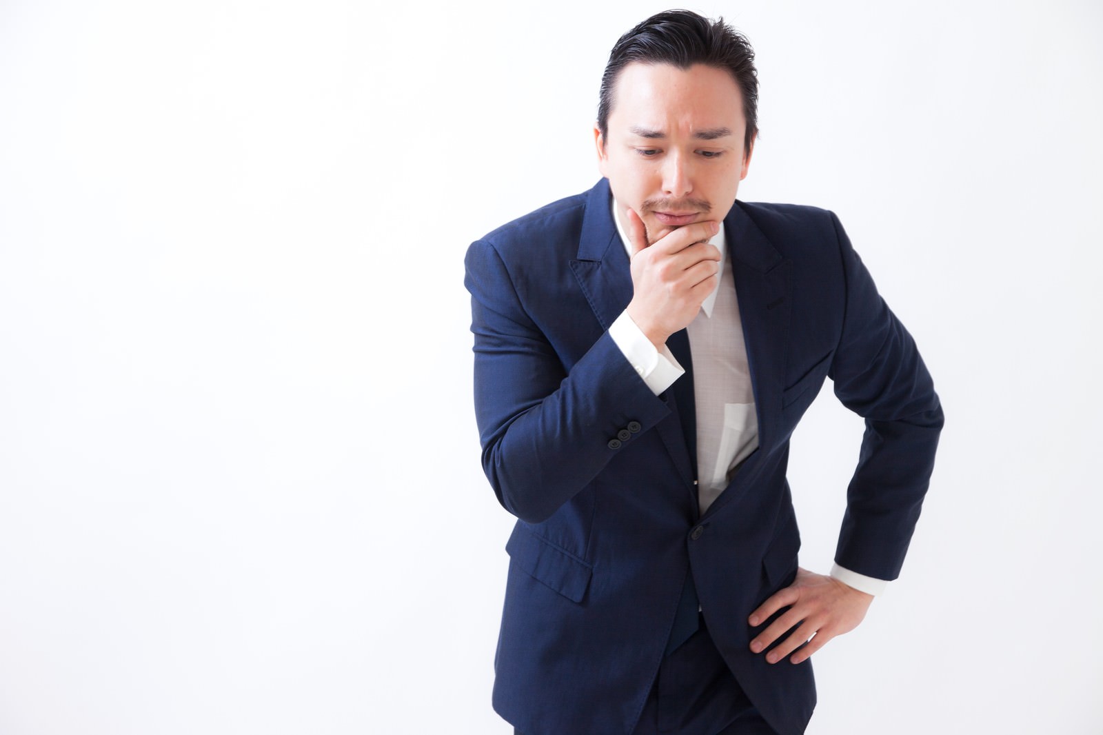 紺色のスーツを着た男性が顔に手を当てて考え込んでいる［モデル：Max_Ezaki］