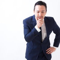 顔に手を当てて考え込む管理職の男性、困惑した表情で思案中の写真