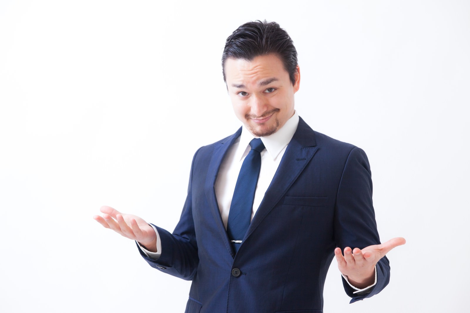 紺色スーツ姿で両手を広げるジェスチャーをする男性。笑顔で疑問を投げかけている［モデル：Max_Ezaki］