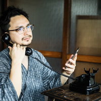 スマホで連絡先を確認しながら古民家の黒電話を使う外国人観光客の写真