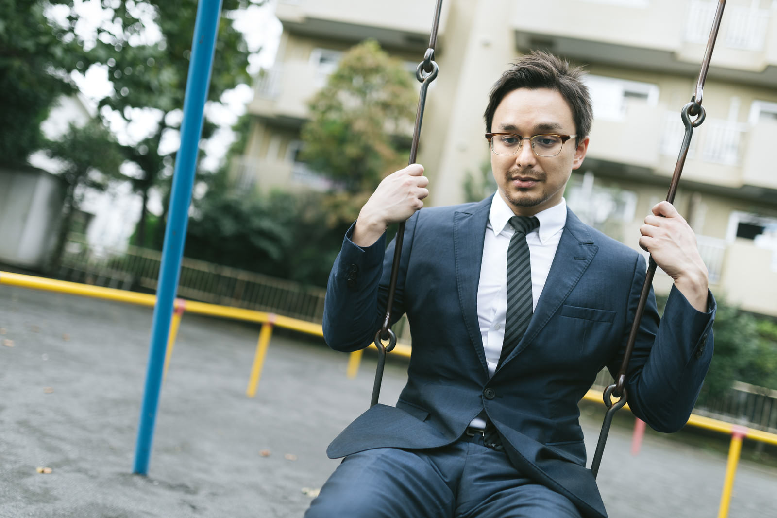 公園のブランコに座るスーツ姿の男性がうつむいている様子［モデル：Max_Ezaki］