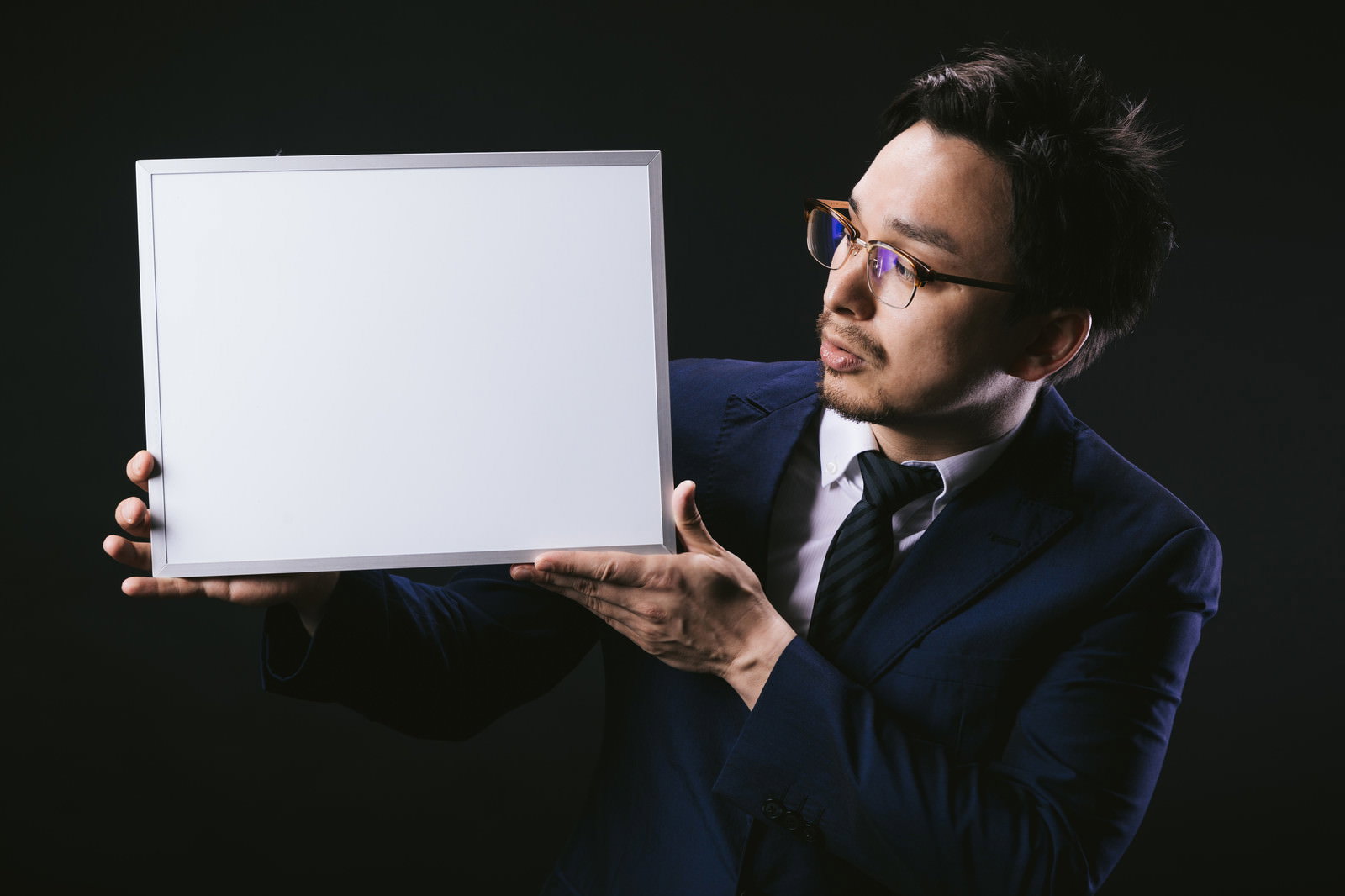 白いボードを両手で持って提示するスーツ姿の男性［モデル：Max_Ezaki］