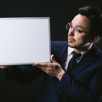 こちらのフリップを御覧ください、とホワイトボードを掲げるスーツ姿の男性の写真