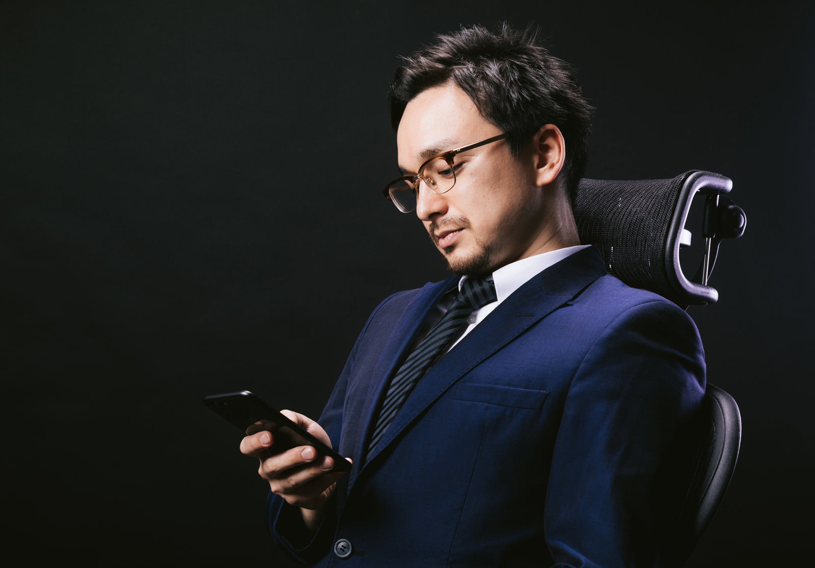 椅子に座ってスマートフォンを見ながらうなだれている男性［モデル：Max_Ezaki］