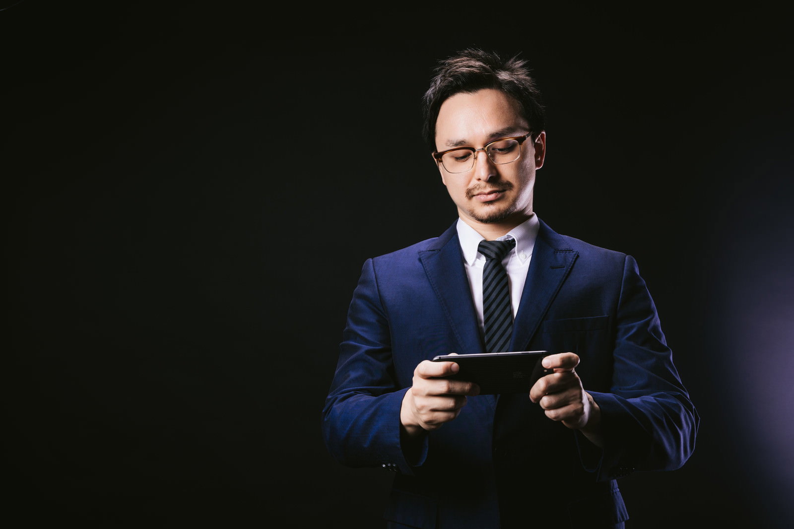 紺色のスーツを着た眼鏡の男性がスマートフォンを見ている［モデル：Max_Ezaki］