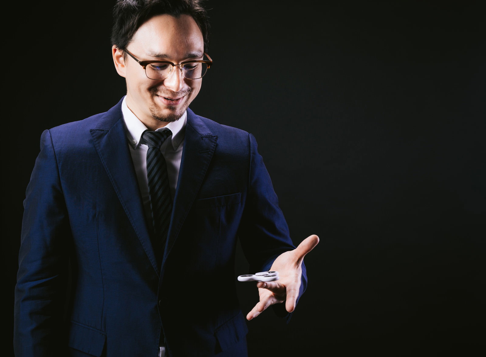 紺色のスーツを着た男性がハンドスピナーを指差している［モデル：Max_Ezaki］